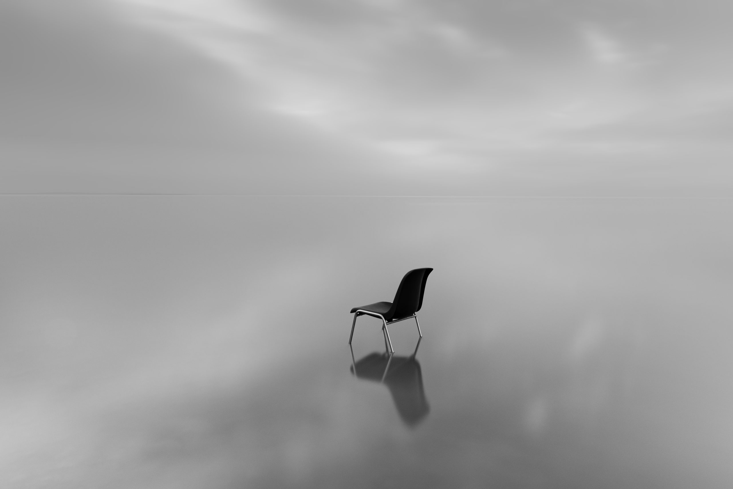 A greyscale shot of a chair on a water surface with a reflection on a rainy day